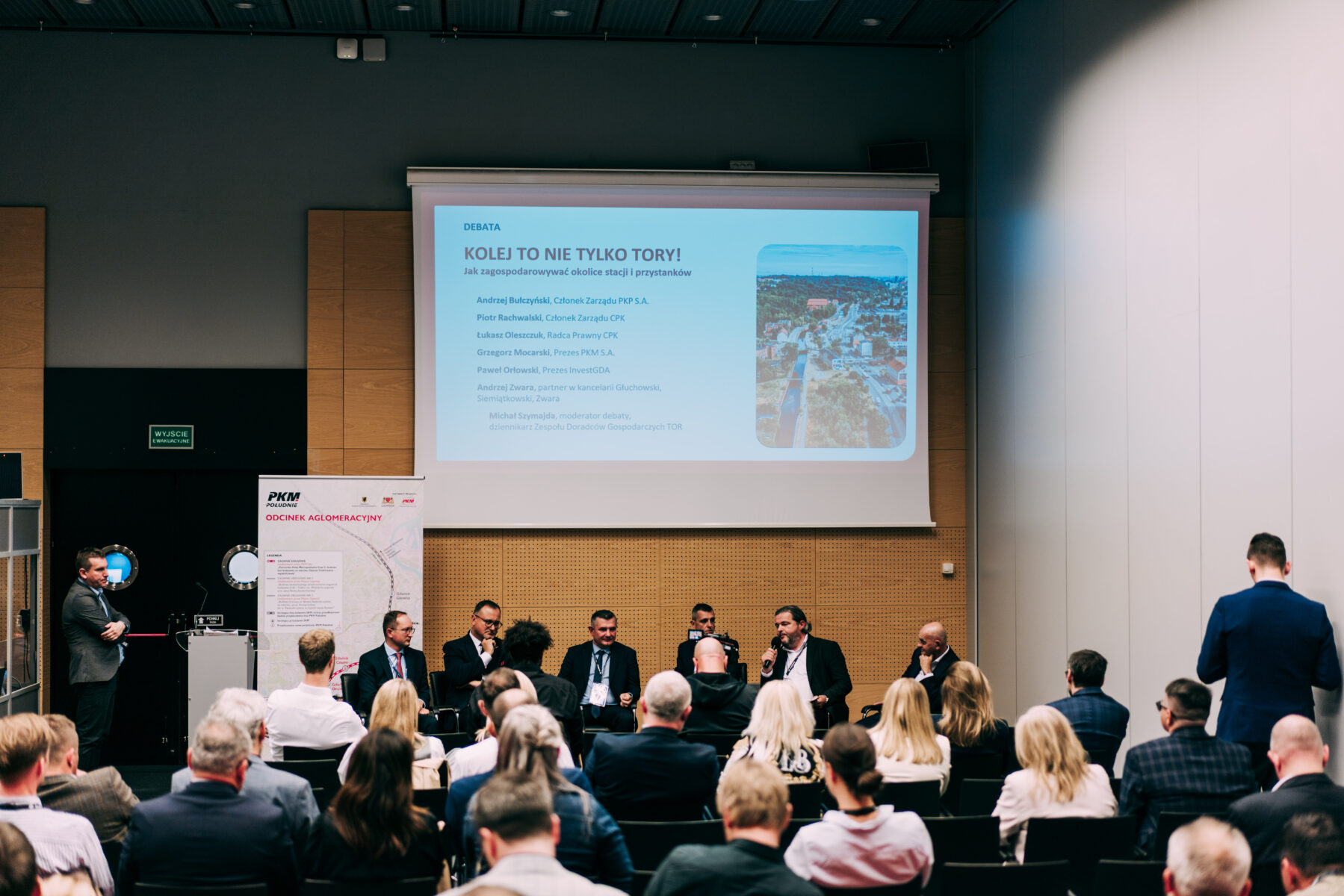 Debata panelowa w sali konferencyjnej. Na ekranie temat "Kolej to nie tylko tory!". Panel ekspertów i publiczność.