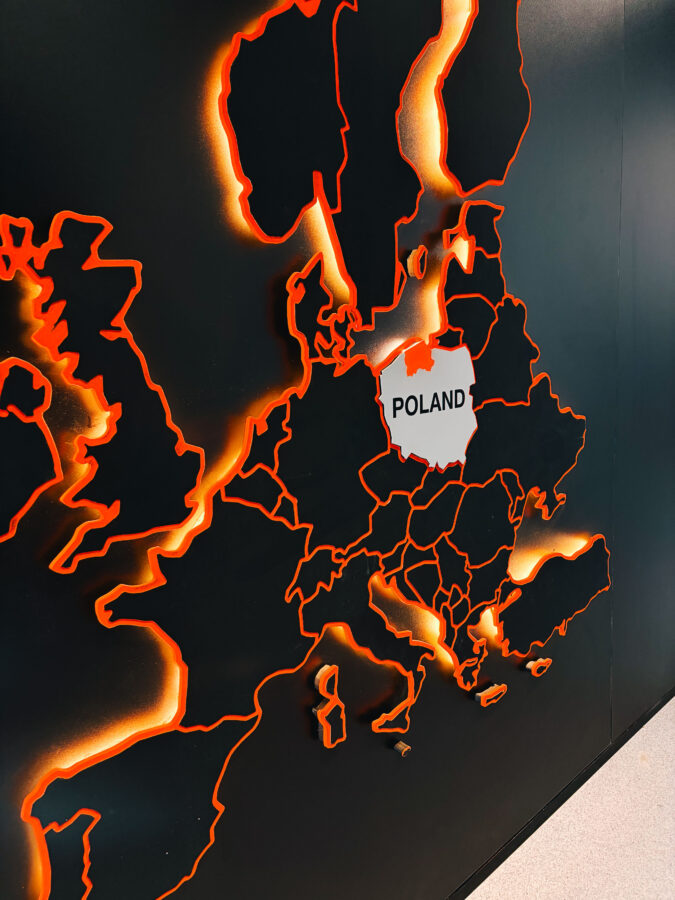 Ciemna mapa Europy z pomarańczowo podświetlonymi konturami. Polska wyróżniona na biało, z napisem "POLAND".