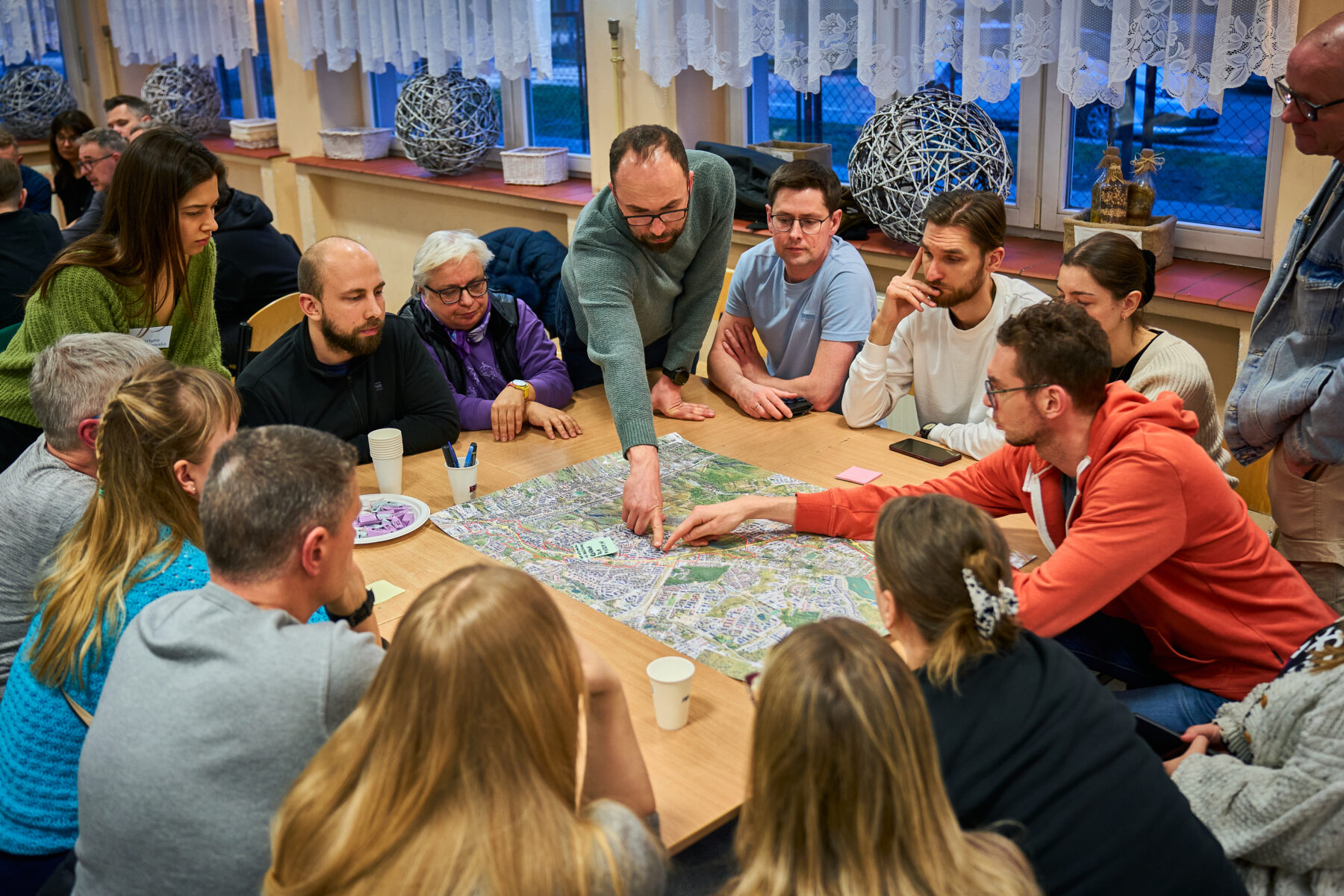 A group of people gathered around a table with a map. Several people are pointing at the map, discussing it.